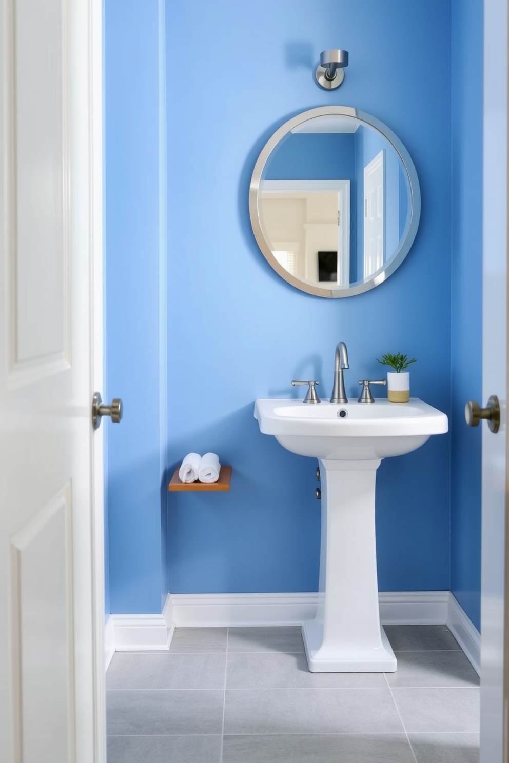 A serene powder room featuring sky blue paint on the walls creates a calming atmosphere. The space includes a sleek white pedestal sink and a round mirror with a brushed nickel frame above it. The floor is adorned with light gray tiles that complement the blue tones. A small wooden shelf holds neatly rolled white towels and a decorative plant, adding a touch of greenery.