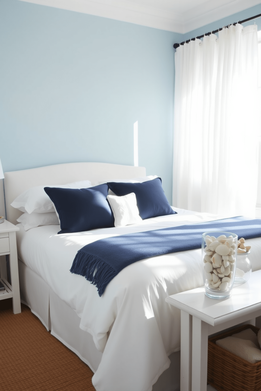 A serene coastal bedroom features a soothing blue and white color palette. The walls are painted in a soft sky blue, and the bedding includes crisp white linens accented with navy blue throw pillows. Natural light floods the room through sheer white curtains, illuminating a comfortable white upholstered bed. A woven jute rug lies beneath the bed, adding texture and warmth to the space. Decorative elements include a collection of seashells displayed in a glass vase on a white nightstand. The overall ambiance is relaxed and inviting, perfect for a coastal retreat.