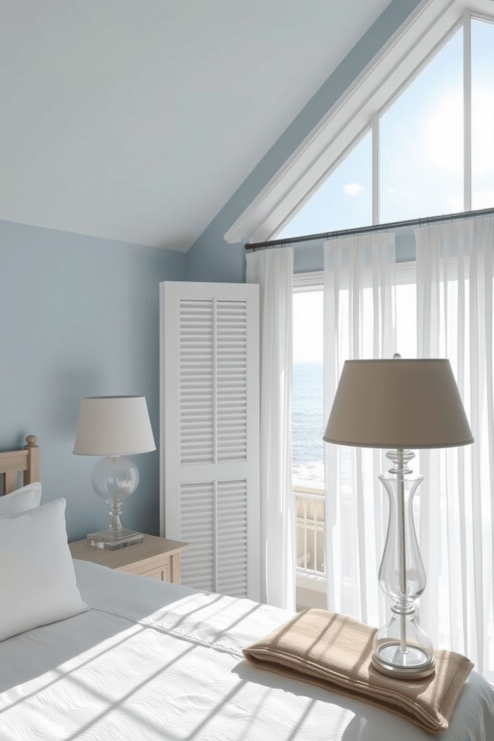 A coastal bedroom filled with natural light featuring glass lamps that emit a soft beachy glow. The walls are painted in a light blue hue, and a large window offers a view of the ocean, allowing the sunlight to filter through sheer white curtains.