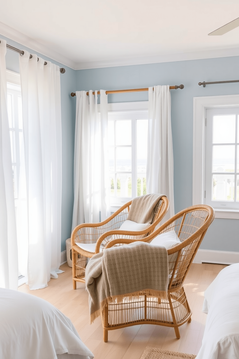 A serene coastal bedroom featuring rattan chairs that evoke a relaxed beach atmosphere. The room is adorned with soft blue walls and light wood flooring, complemented by airy white curtains that flutter gently in the breeze. The rattan chairs are positioned near a large window, allowing natural light to fill the space. A cozy, neutral-colored throw blanket drapes over one chair, enhancing the inviting and tranquil feel of the room.