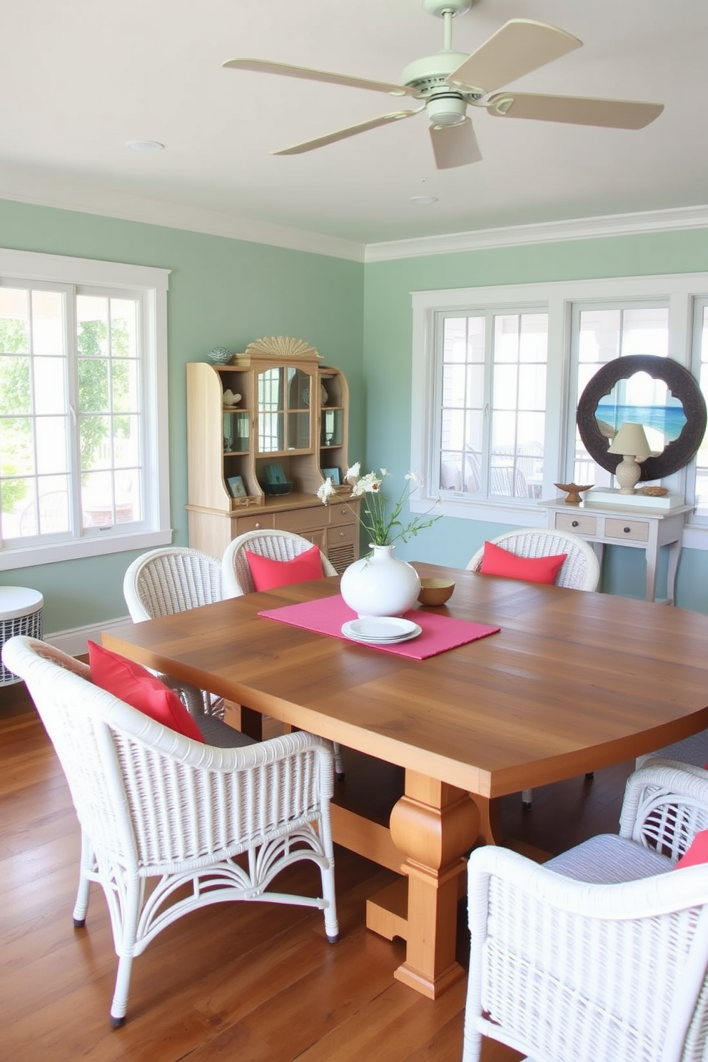 A coastal dining room features a large wooden table with a natural finish surrounded by white wicker chairs. Bright coral accents are incorporated through vibrant cushions and a table runner, adding a lively pop of color to the serene coastal theme. The walls are painted in a soft seafoam green, creating a calming backdrop. Large windows allow natural light to flood the space, while ocean-inspired decor pieces enhance the coastal aesthetic.