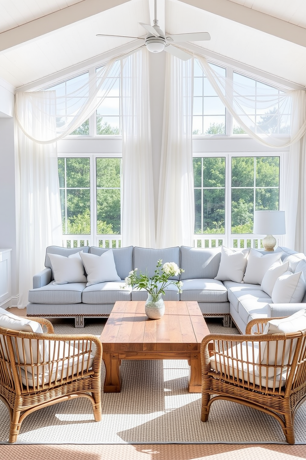 A bright and airy coastal living room filled with natural light. Breezy sheer curtains frame the large windows, gently billowing in the sea breeze, creating a soft and inviting atmosphere. The room features a comfortable sectional sofa upholstered in light blue fabric, complemented by white and sandy beige throw pillows. A reclaimed wood coffee table sits at the center, surrounded by woven rattan chairs that enhance the coastal vibe.