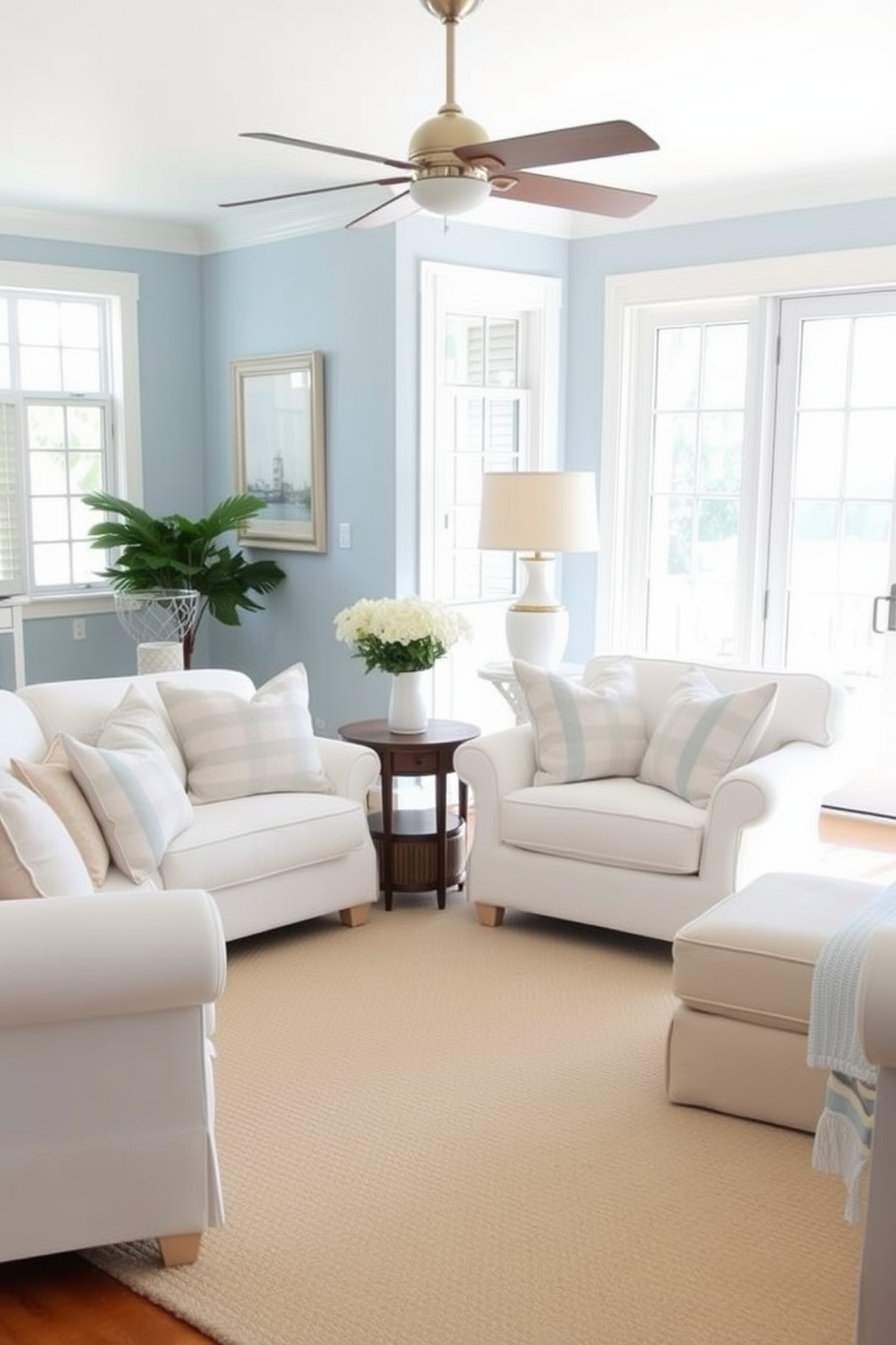 A coastal living room featuring nautical stripes on throw pillows. The space is bright and airy with large windows allowing natural light to flood in. The walls are painted in a soft blue hue, complementing the white furniture. A light-colored, textured rug anchors the seating area, creating a cozy atmosphere.