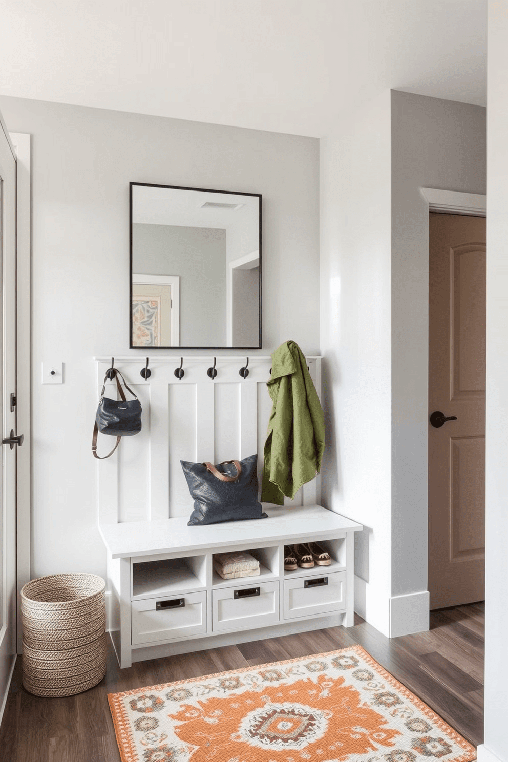 A functional entryway featuring built-in storage solutions. A sleek bench with hidden compartments is positioned against the wall, complemented by a row of stylish hooks for coats and bags. The walls are painted in a light gray tone, enhancing the spacious feel of the area. A large mirror above the bench reflects natural light, while a decorative rug adds warmth and texture to the space.