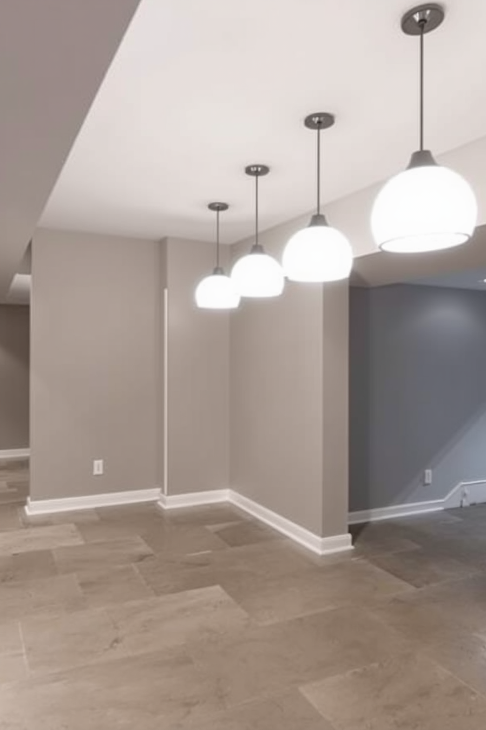 A contemporary basement design featuring bright pendant lights that add a stylish touch to the space. The walls are painted in a soft gray, and the flooring is a sleek polished concrete, creating a modern and inviting atmosphere.