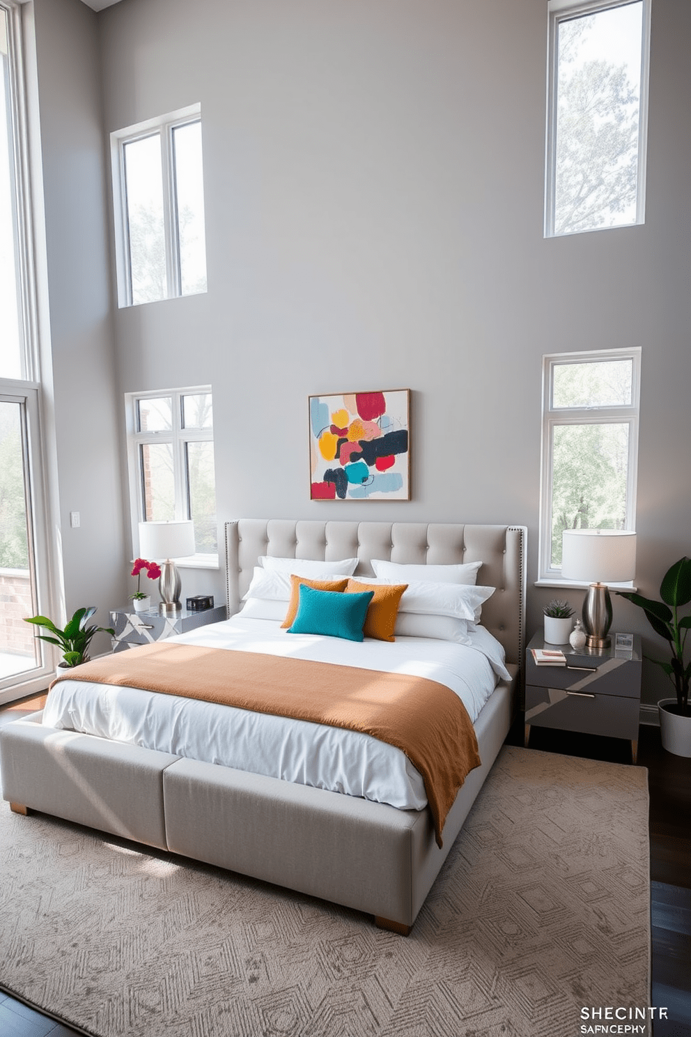 A contemporary bedroom featuring a large upholstered bed with crisp white linens and colorful accent pillows. Floor-to-ceiling windows allow natural light to flood the space, complemented by potted plants placed strategically around the room for a fresh vibe. The walls are painted in a soft gray tone, creating a calming atmosphere. A sleek nightstand with a modern lamp sits on either side of the bed, while an abstract piece of artwork hangs above the headboard.