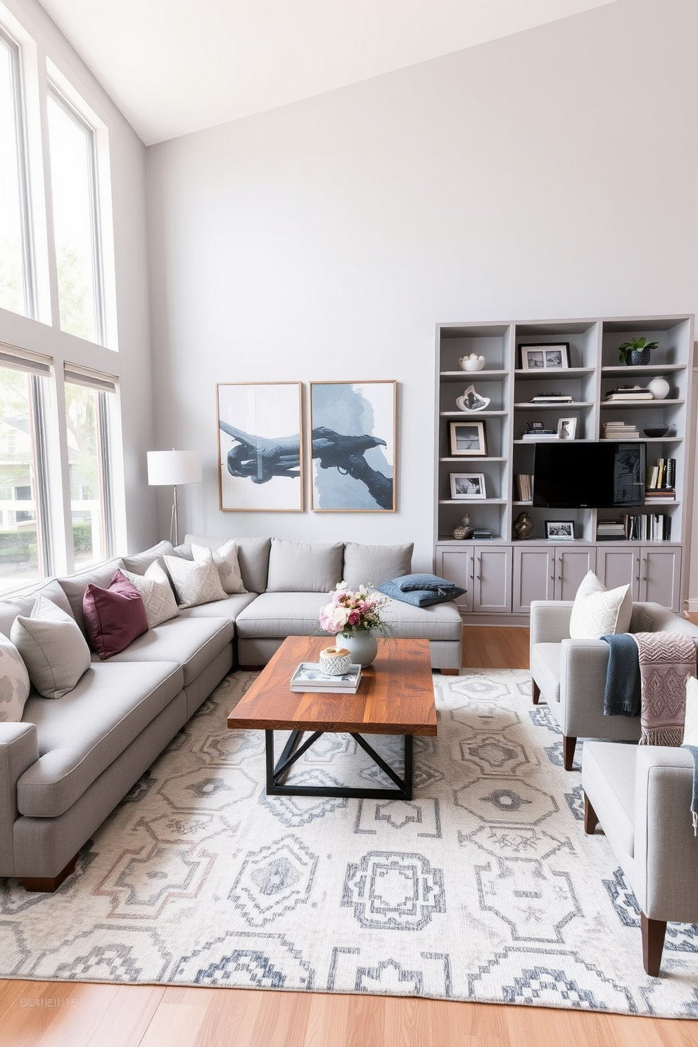 A contemporary family room featuring a cohesive color scheme of soft grays and muted blues. The space includes a plush sectional sofa adorned with decorative pillows, a sleek coffee table made of reclaimed wood, and a large area rug that ties the colors together. The walls are painted in a light gray tone, complemented by abstract art pieces that add a pop of color. Large windows allow natural light to flood the room, enhancing the inviting atmosphere and showcasing a stylish bookshelf filled with curated decor and family photos.