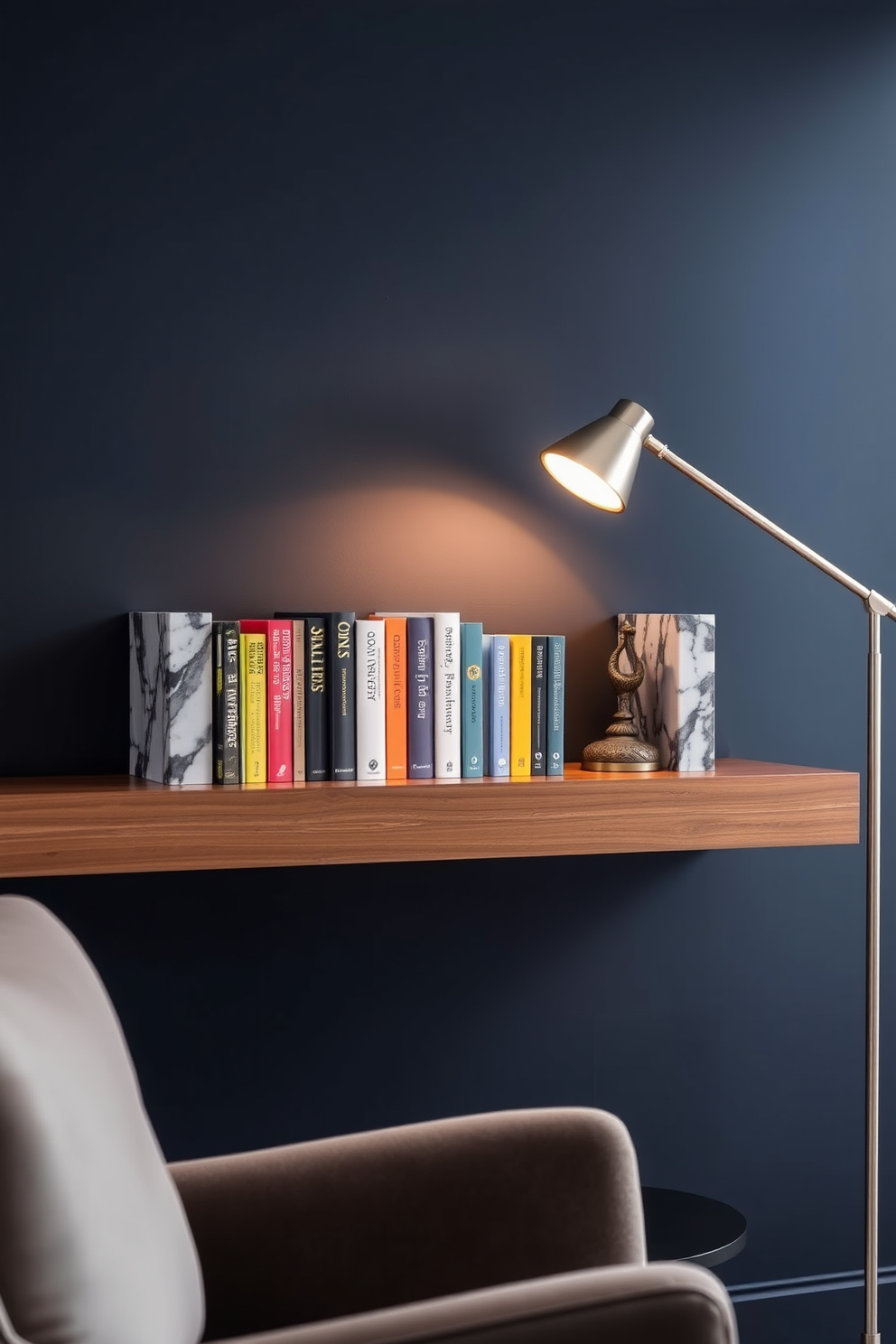 Stylish bookends made of polished marble flank a row of colorful books on a sleek wooden shelf. The backdrop features a wall painted in a deep navy blue, enhancing the elegance of the space. A cozy reading nook is created with a plush armchair and a small side table beside the shelf. Soft ambient lighting from a modern floor lamp casts a warm glow, inviting relaxation and enjoyment of the collection.