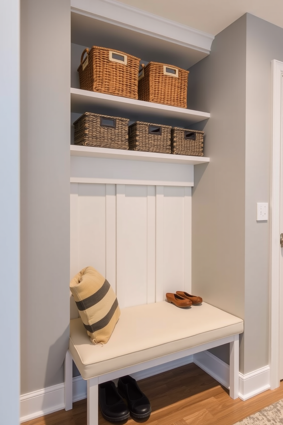 A contemporary mudroom features decorative baskets neatly arranged on open shelves, providing stylish organization for shoes and outdoor gear. The walls are painted in a soft gray, complemented by a sleek bench with a cushioned seat, creating a welcoming and functional space.