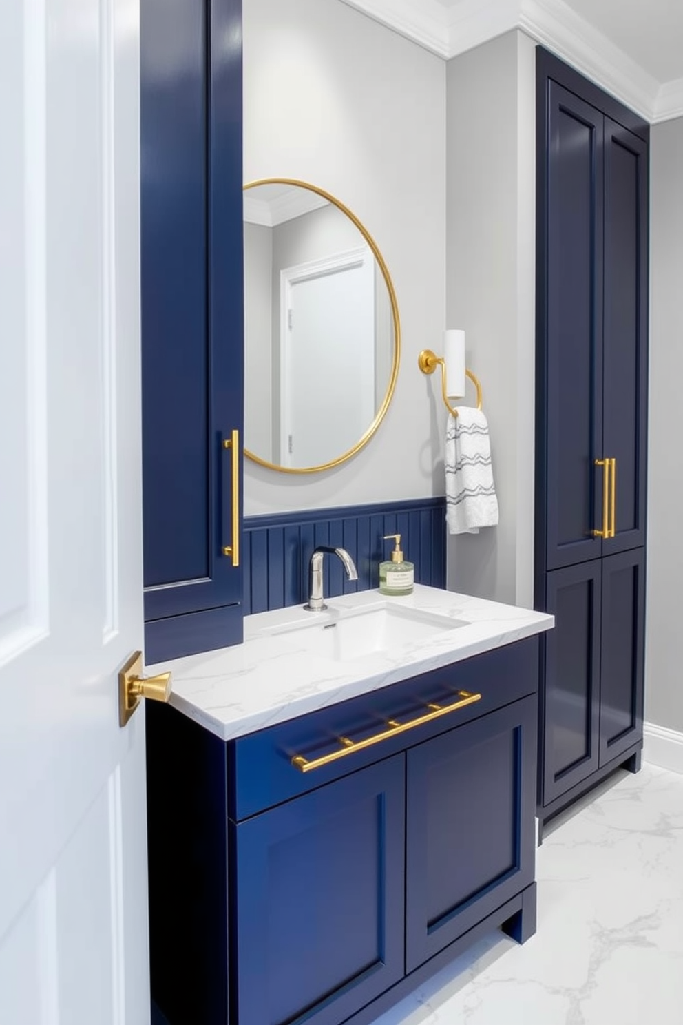 Bold accent colors on cabinetry create a striking focal point in a contemporary powder room. The cabinetry features a deep navy blue finish, contrasting beautifully with the light gray walls and white marble flooring. Sleek gold hardware complements the bold cabinetry, adding a touch of luxury to the space. A round mirror with a thin gold frame hangs above a modern sink, enhancing the room's sophisticated aesthetic.