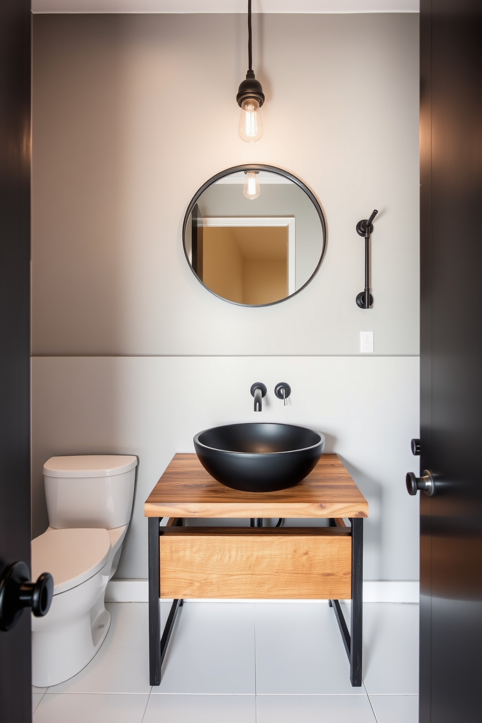 A contemporary powder room featuring industrial fixtures that contrast with smooth surfaces. The walls are painted in a soft gray, and the floor is covered with large white tiles for a clean look. A sleek black sink is mounted on a reclaimed wood vanity, adding warmth to the space. Above the sink, a round mirror with an exposed bulb light fixture enhances the industrial aesthetic.