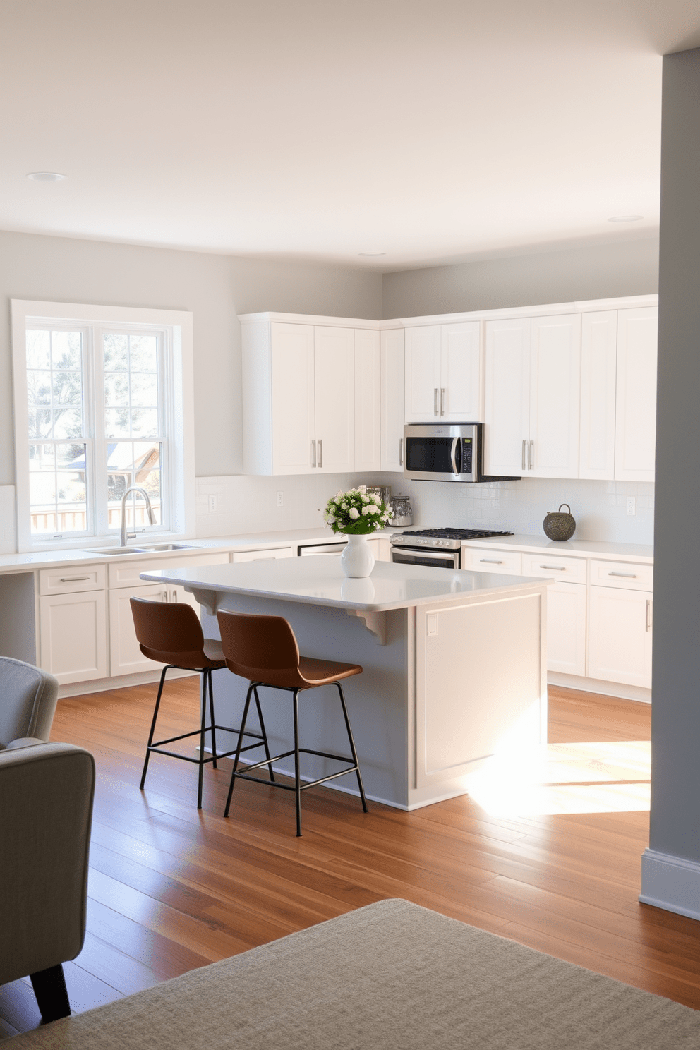 A corner island features a sleek countertop with seating options for casual dining. Surrounding the island, the kitchen showcases modern cabinetry in a soft white finish and stainless steel appliances for a contemporary look. Natural light floods the space through large windows, highlighting the warm wooden floors. The walls are painted in a light gray hue, creating a fresh and inviting atmosphere.