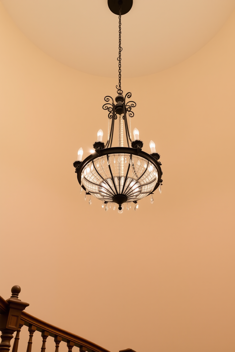 A stunning vintage chandelier hangs gracefully above a grand curved staircase, casting a warm and inviting glow. The staircase features elegant wood railings and intricate balusters, complementing the timeless charm of the chandelier.