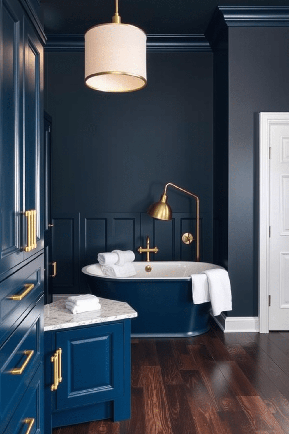 Deep navy cabinetry with brass accents creates a dramatic and elegant atmosphere. The walls are painted in a rich charcoal gray, enhancing the depth of the space. A freestanding soaking tub sits in the center, surrounded by plush white towels and a sleek brass floor lamp. The floor features dark wood planks that add warmth and contrast to the overall design.