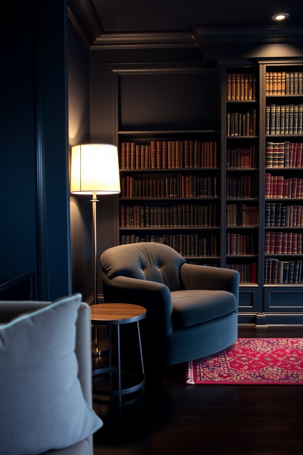 A cozy reading nook nestled in a dark study room. The walls are painted a deep navy blue, and a plush, oversized armchair in charcoal gray sits in the corner, accompanied by a small round side table. A tall bookshelf filled with dark wood and leather-bound books lines one wall. Soft, warm lighting from a stylish floor lamp creates an inviting atmosphere, while a rich, patterned area rug adds texture to the dark hardwood floor.