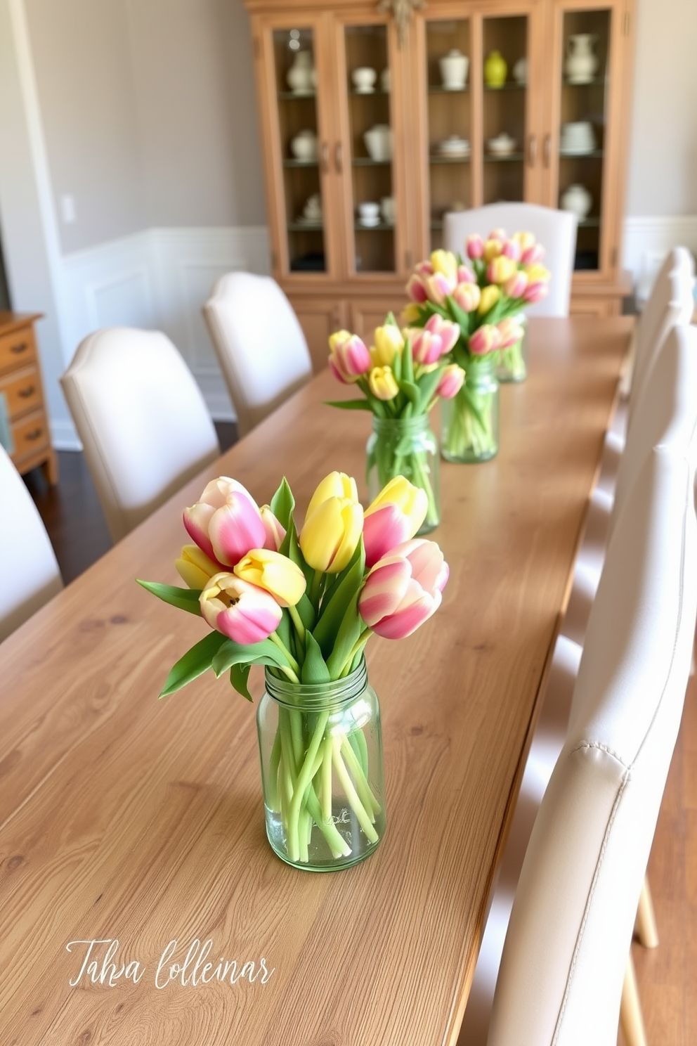 Fresh tulips in mason jars serve as vibrant centerpieces on a long wooden dining table. Surrounding the table are elegant upholstered chairs in soft pastel colors, enhancing the festive Easter atmosphere.