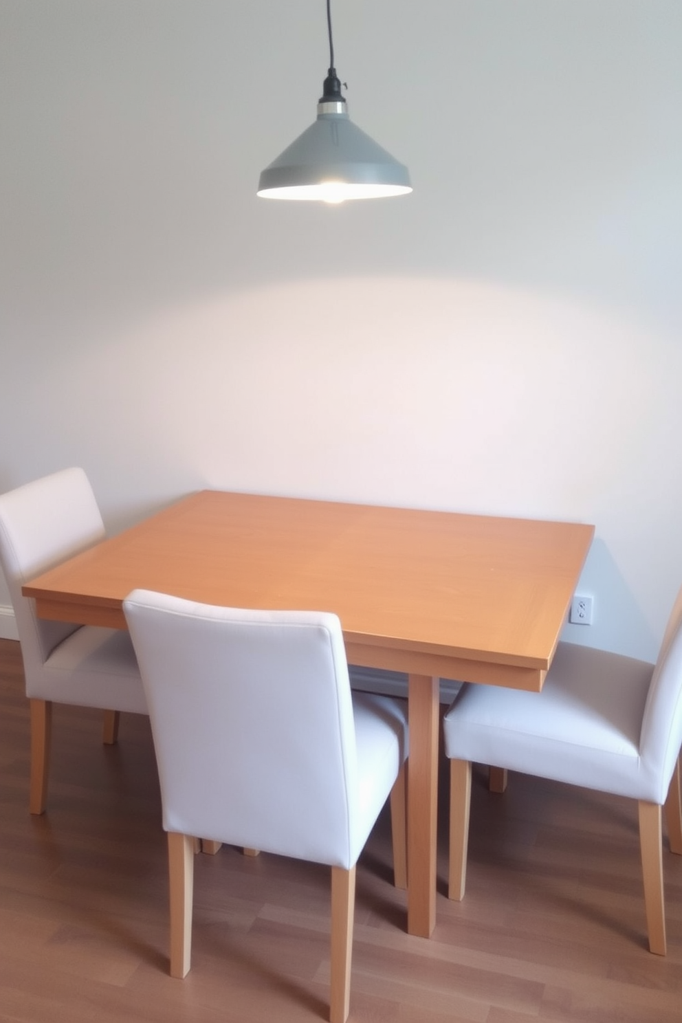 A simple drop-leaf dining table is positioned against a light gray wall, providing a versatile space for dining and entertaining. The table is made of natural wood with a smooth finish, and when expanded, it comfortably seats four guests. Surrounding the table are four upholstered chairs in a soft pastel color, adding a touch of warmth to the room. A stylish pendant light hangs above the table, casting a warm glow that enhances the inviting atmosphere.