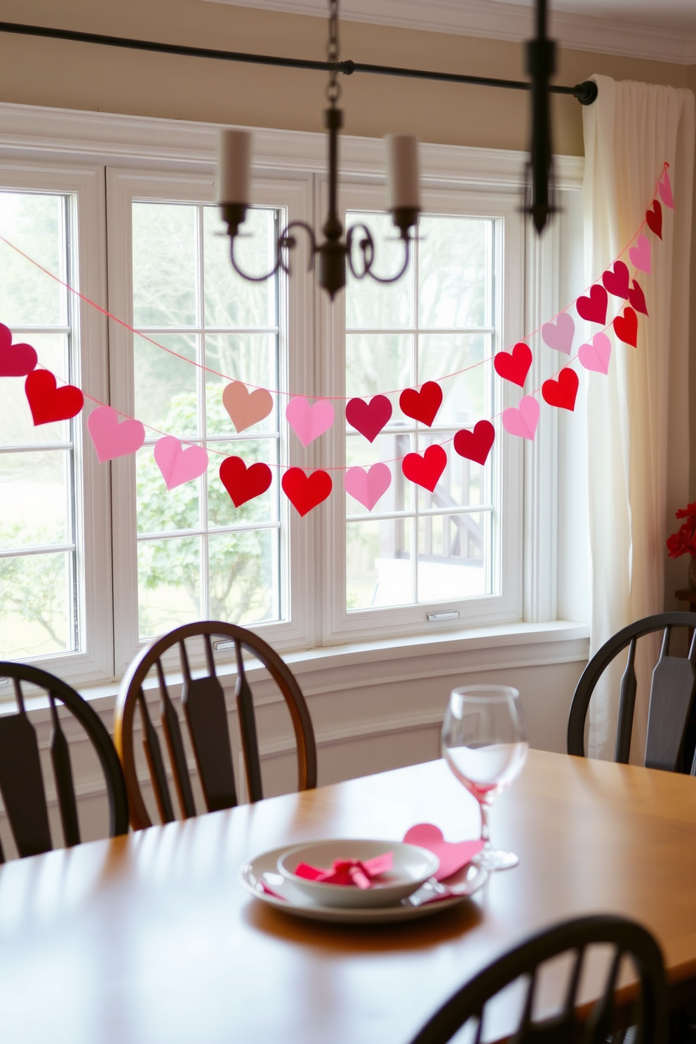 A charming dining room adorned with a DIY heart garland that hangs gracefully across the window. The garland features an array of red and pink paper hearts, creating a festive atmosphere perfect for Valentine's Day celebrations.