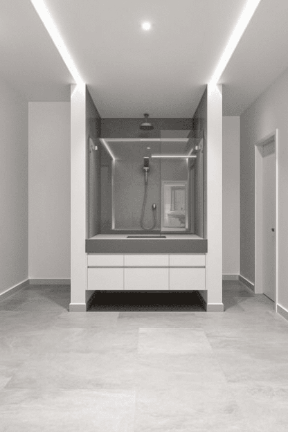 A minimalist bathroom design featuring sleek lines and a spacious layout. The walls are painted in a soft white hue, and the floor is covered with large format gray tiles for a seamless look. In the center, a floating vanity with a solid surface countertop offers ample storage without the need for decorative moldings. A frameless glass shower enclosure showcases a rain showerhead and a simple, elegant faucet.