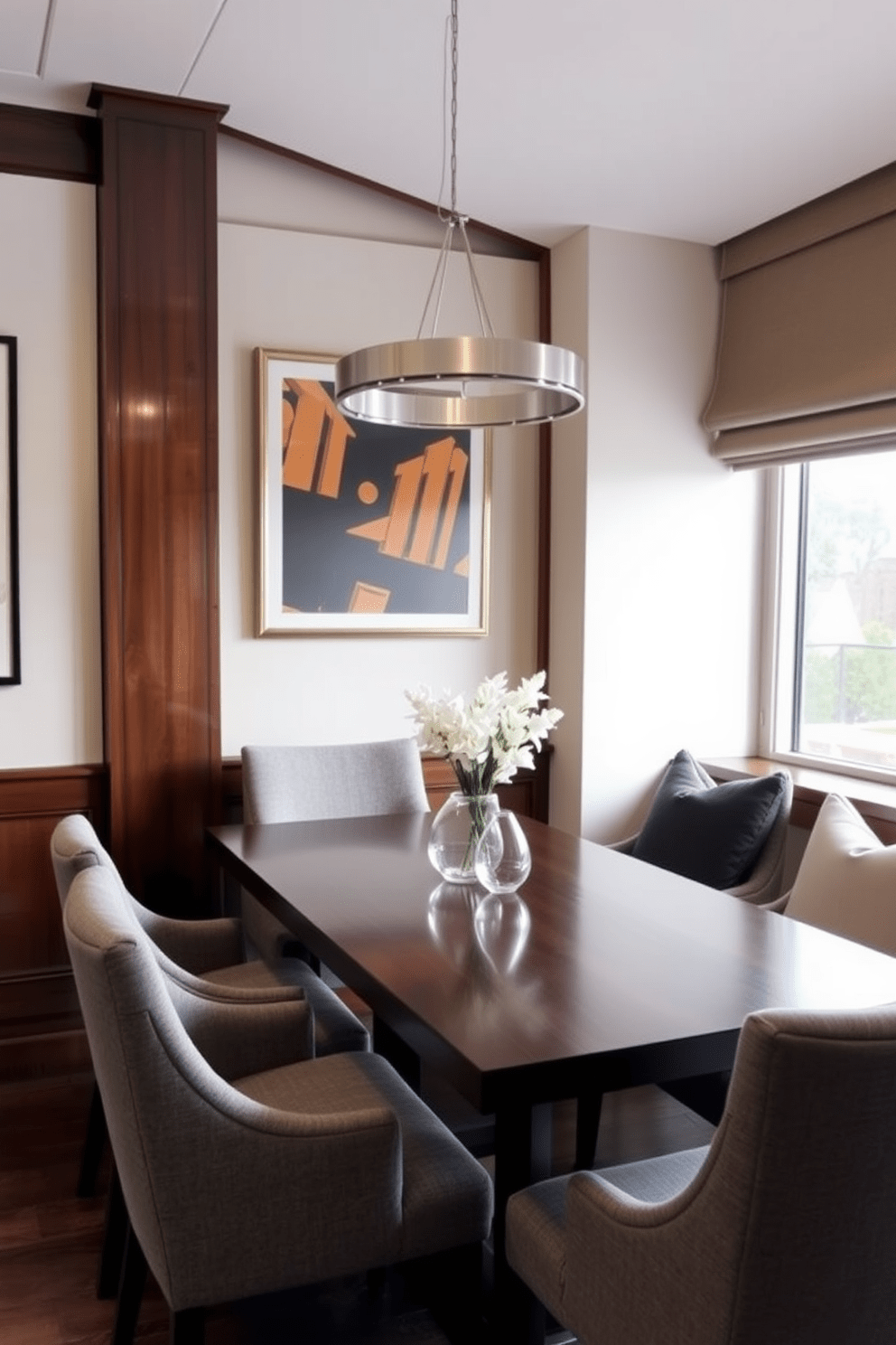 Refined dining area with stylish seating. The table is made of dark wood with a polished finish, surrounded by upholstered chairs in a soft gray fabric. A modern chandelier hangs above, casting a warm glow over the space. The walls are adorned with tasteful artwork, and a large window allows natural light to fill the room.