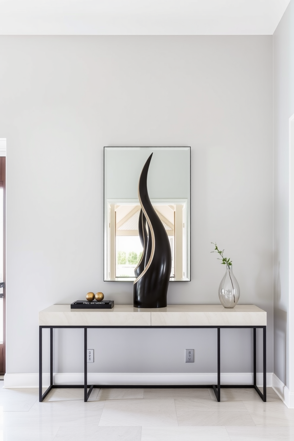 Artistic sculpture for a modern vibe. The entrance foyer features a sleek, minimalist design with a striking abstract sculpture as the focal point. The walls are painted in a soft gray, creating a neutral backdrop that enhances the sculpture's visual impact. A contemporary console table sits beneath a large mirror, reflecting natural light and adding depth to the space.