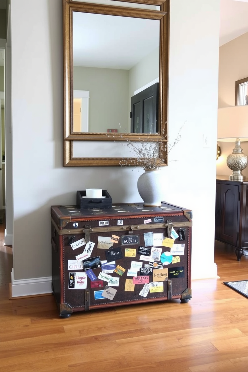 A vintage trunk is placed against the wall in the entrance foyer, serving as a stylish storage solution. The trunk is adorned with travel stickers, adding character and charm to the space. The foyer features a warm wood floor and soft lighting that highlights the trunk. A large mirror hangs above the trunk, reflecting the inviting atmosphere of the entrance.