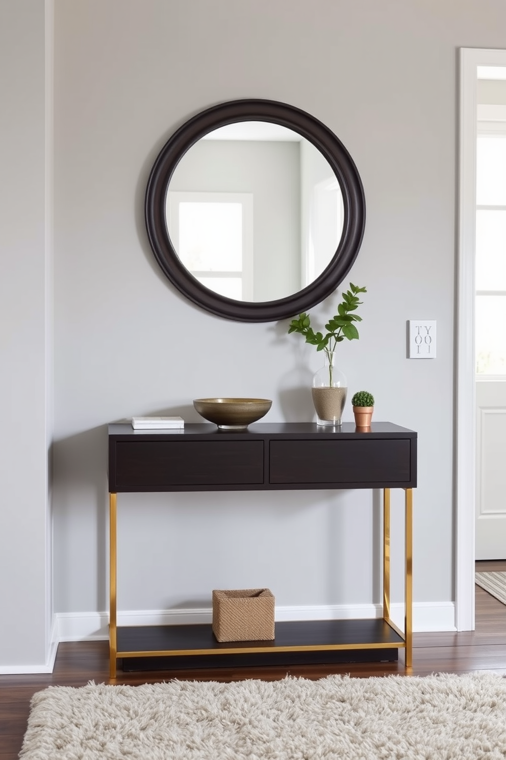 A stylish entryway featuring a sleek console table made of dark wood with gold accents. Above the table, a large round mirror reflects natural light, while a decorative bowl and a small potted plant add a touch of greenery. The walls are painted in a soft gray hue, creating a calming atmosphere. A plush area rug in neutral tones lies beneath the table, providing warmth and texture to the space.