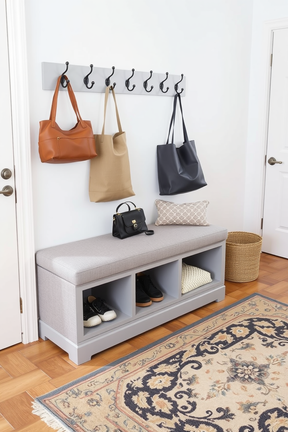 A stylish entryway featuring a small bench with storage options positioned against the wall. The bench is upholstered in a soft gray fabric, providing a comfortable seat while also offering hidden compartments for shoes and accessories. On the floor, a beautiful area rug adds warmth and texture, while the walls are painted in a crisp white to enhance the space. A set of hooks is mounted above the bench for hanging coats and bags, creating an organized and inviting atmosphere.