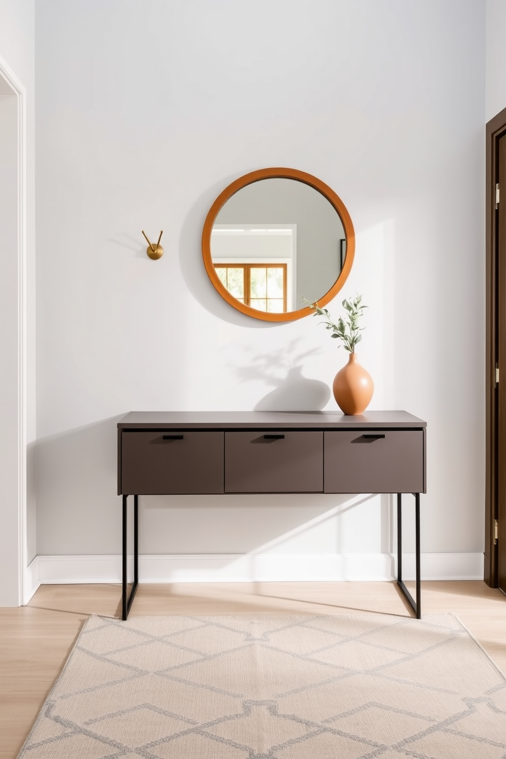 A welcoming entryway featuring a sleek console table against a light gray wall. Above the table, decorative wall hooks in an elegant brass finish provide functionality while adding a touch of style. The floor is adorned with a soft area rug in muted tones that complement the overall color scheme. A round mirror with a wooden frame hangs above the console table, reflecting natural light and enhancing the space's openness.