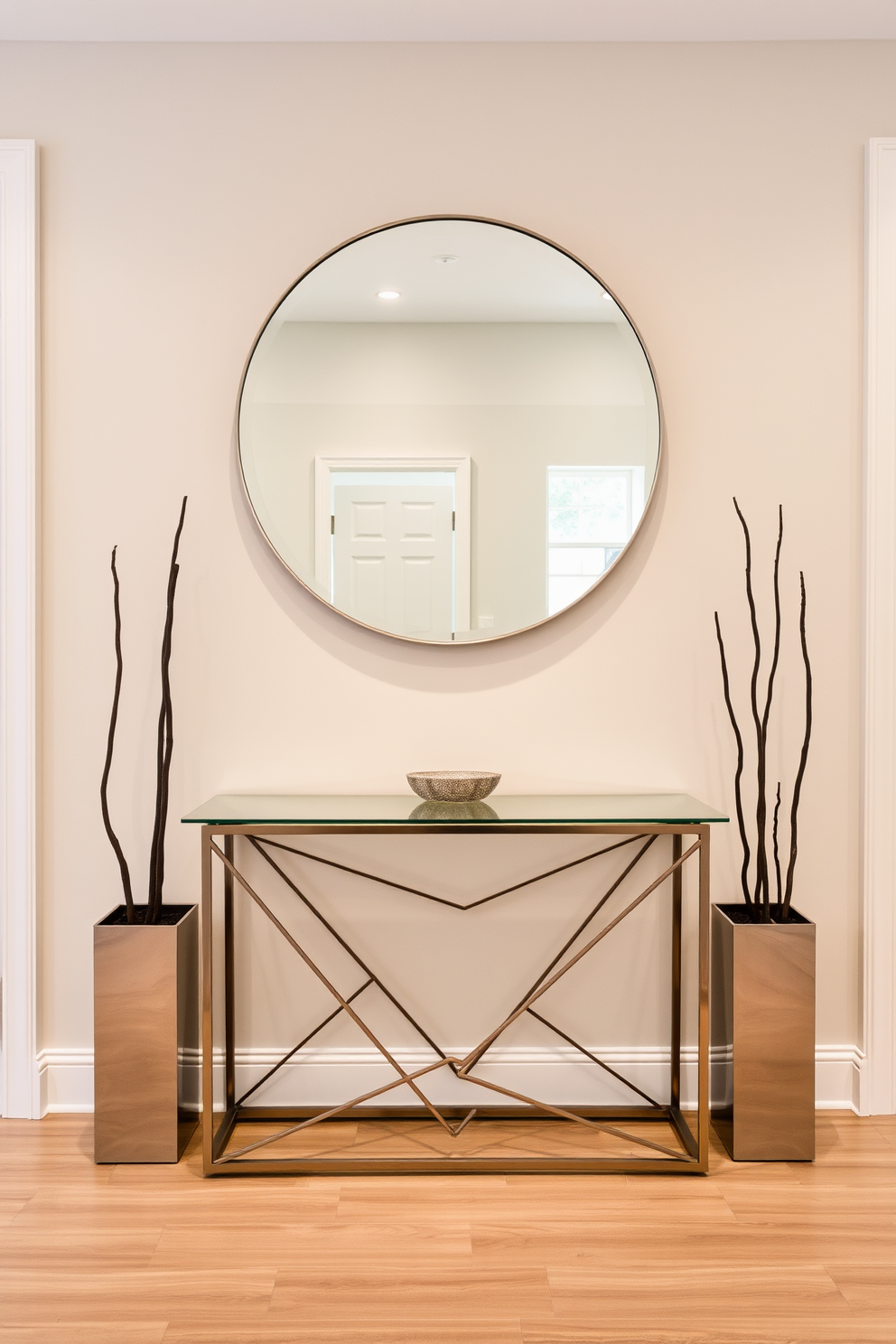 A modern entryway featuring a sleek console table with a geometric design. The table is made of metal and glass, providing a contemporary aesthetic that complements the surrounding decor. On top of the table, a large round mirror reflects the light, enhancing the space's openness. Flanking the table are two minimalist planters with tall, sculptural plants that add a touch of greenery.