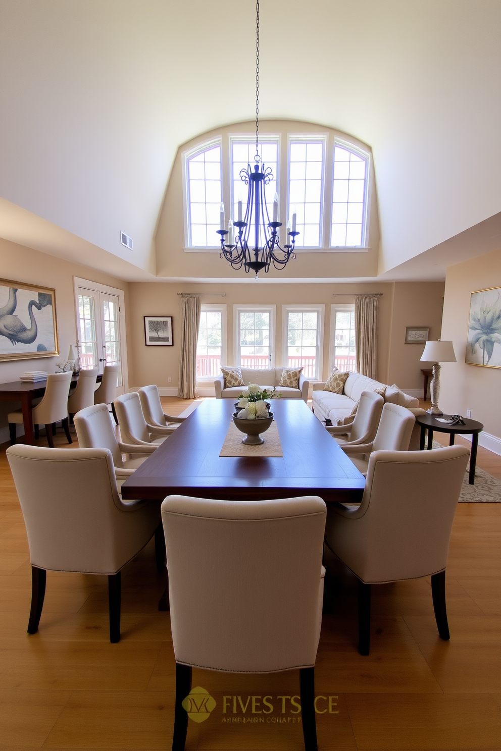 A spacious open concept dining and living area features a large wooden dining table surrounded by upholstered chairs in soft pastel colors. The living space includes a plush sectional sofa adorned with decorative cushions and a stylish coffee table at the center. Natural light floods the room through expansive windows, highlighting the elegant chandelier above the dining table. The walls are painted in a warm neutral tone, complemented by artwork that adds a touch of sophistication to the ambiance.