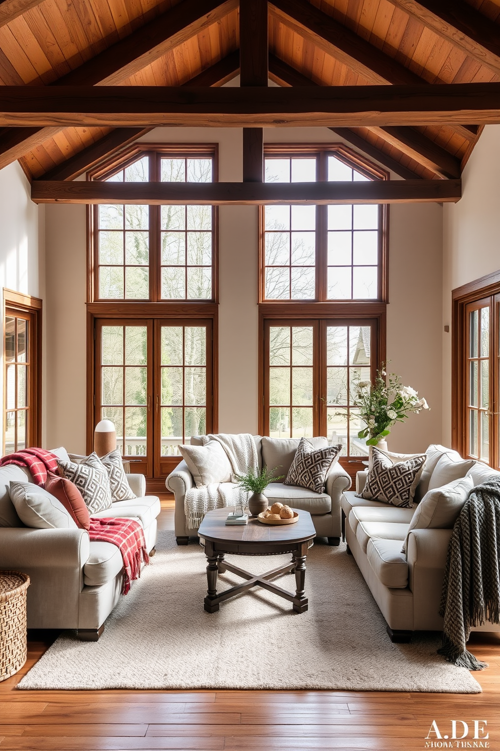 A cozy European family room featuring plush sofas adorned with textured throw blankets in various shades. Large windows allow natural light to flood the space, highlighting the warm wooden beams and soft area rug underfoot.