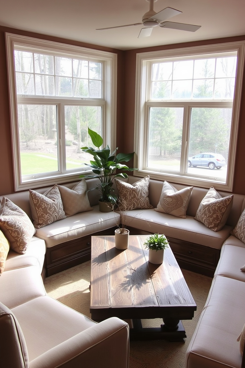 A cozy seating nook designed with built-in benches upholstered in soft, neutral fabric. The space features large windows that allow natural light to flood in, creating an inviting atmosphere for family gatherings. The walls are adorned with warm, earthy tones, complemented by decorative throw pillows in various patterns. A rustic wooden coffee table sits at the center, surrounded by potted plants that enhance the room's charm.