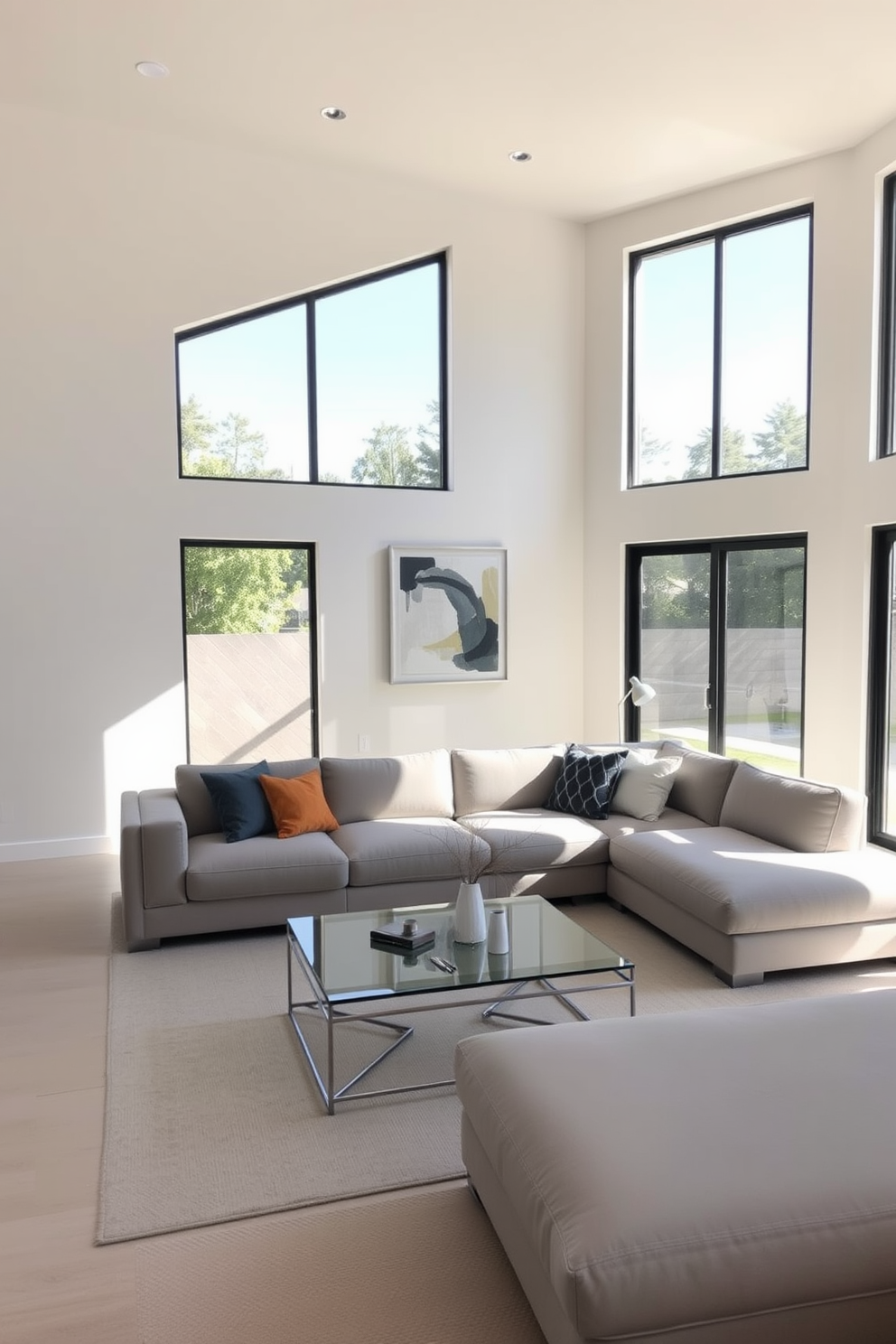 A sleek modern family room features clean lines and a neutral color palette. The space includes a low-profile sectional sofa in soft gray and a minimalist coffee table made of glass and metal. Large windows allow natural light to flood the room, highlighting the simplicity of the decor. A single piece of abstract art hangs on the wall, and a few carefully chosen decorative pillows add a pop of color.