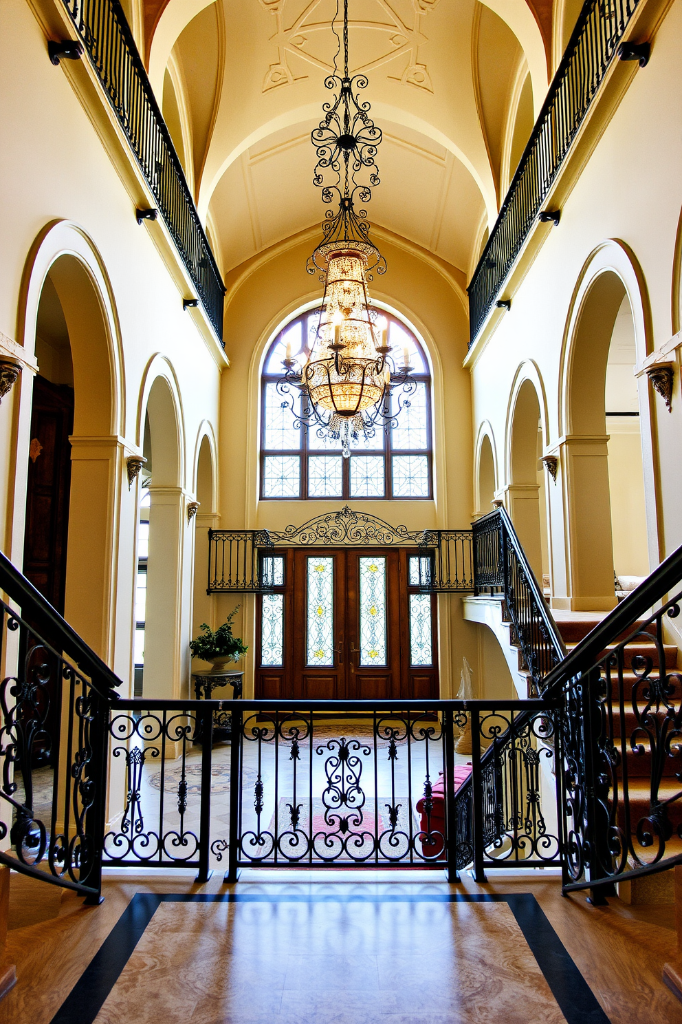 A grand European foyer featuring elegant wrought iron railings that add a classic touch to the space. The foyer is adorned with a stunning chandelier hanging from a high ceiling, illuminating the intricate details of the wrought iron work.