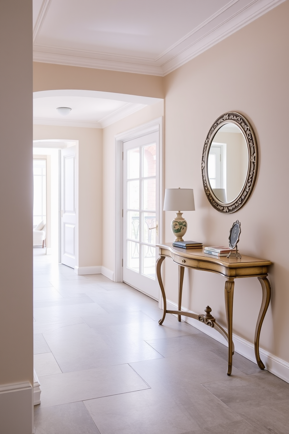 A serene European foyer featuring a subtle color palette. The walls are painted in soft beige, complemented by a light gray stone floor that exudes elegance. An antique console table sits against one wall, adorned with a small decorative lamp and a few art books. A large round mirror with a delicate silver frame hangs above the table, reflecting the natural light that floods the space.