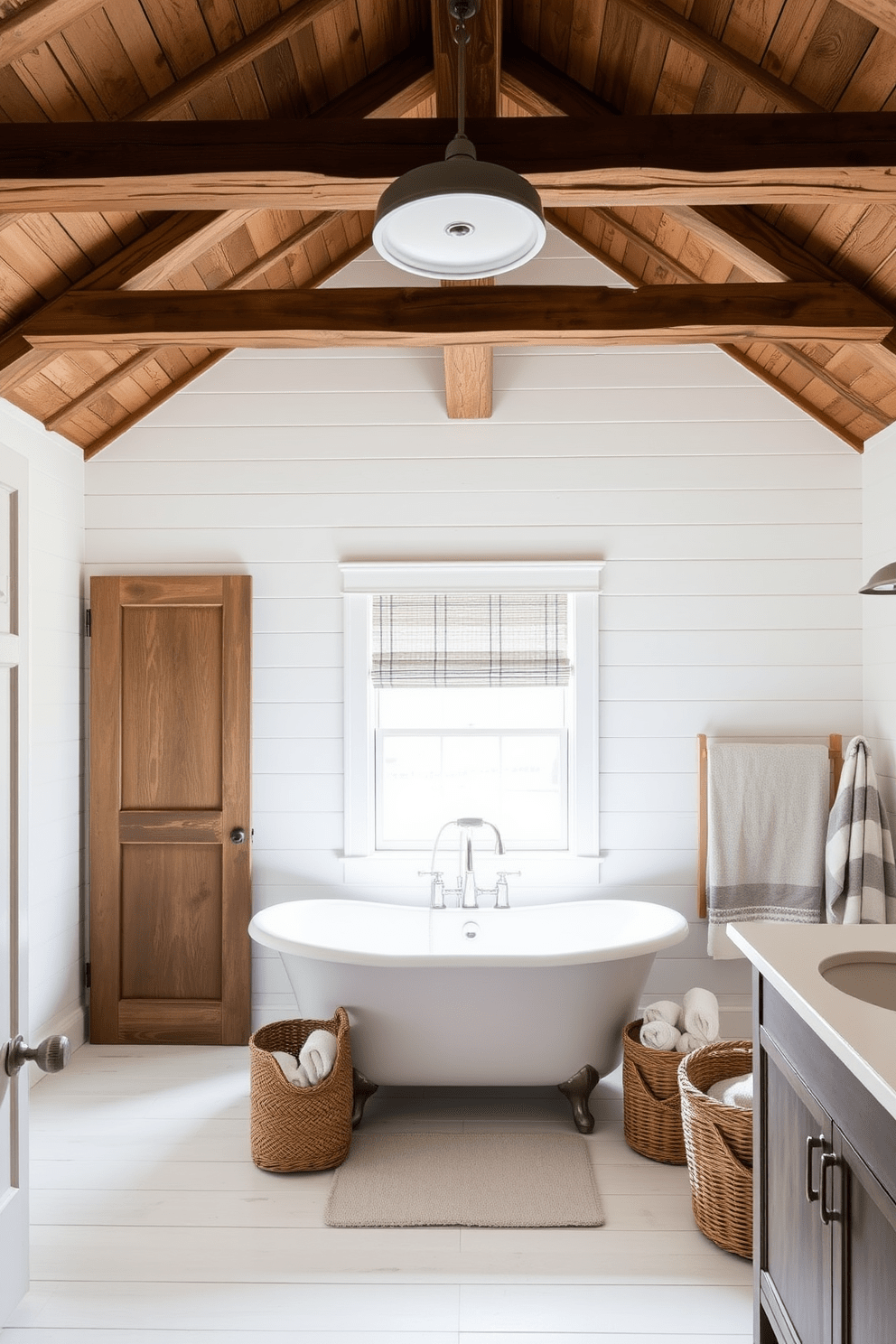 A cozy farmhouse bathroom features a rustic wood beam ceiling that adds warmth and character to the space. The walls are shiplap painted in soft white, complementing the natural wood tones of the beams. The bathroom showcases a freestanding soaking tub positioned beneath a window, allowing natural light to flood the room. Vintage-inspired fixtures in brushed nickel enhance the farmhouse aesthetic, while a woven basket holds plush towels nearby.