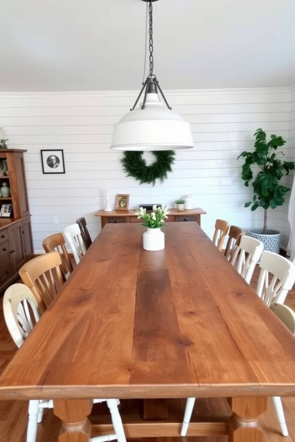 A rustic wood table with a weathered finish takes center stage in a cozy farmhouse dining room. Surrounding the table are mismatched chairs, each with its own unique charm, adding to the inviting and eclectic atmosphere. The walls are adorned with shiplap, painted in a soft white hue that complements the natural wood tones. A large farmhouse-style pendant light hangs above the table, casting a warm glow over the space.