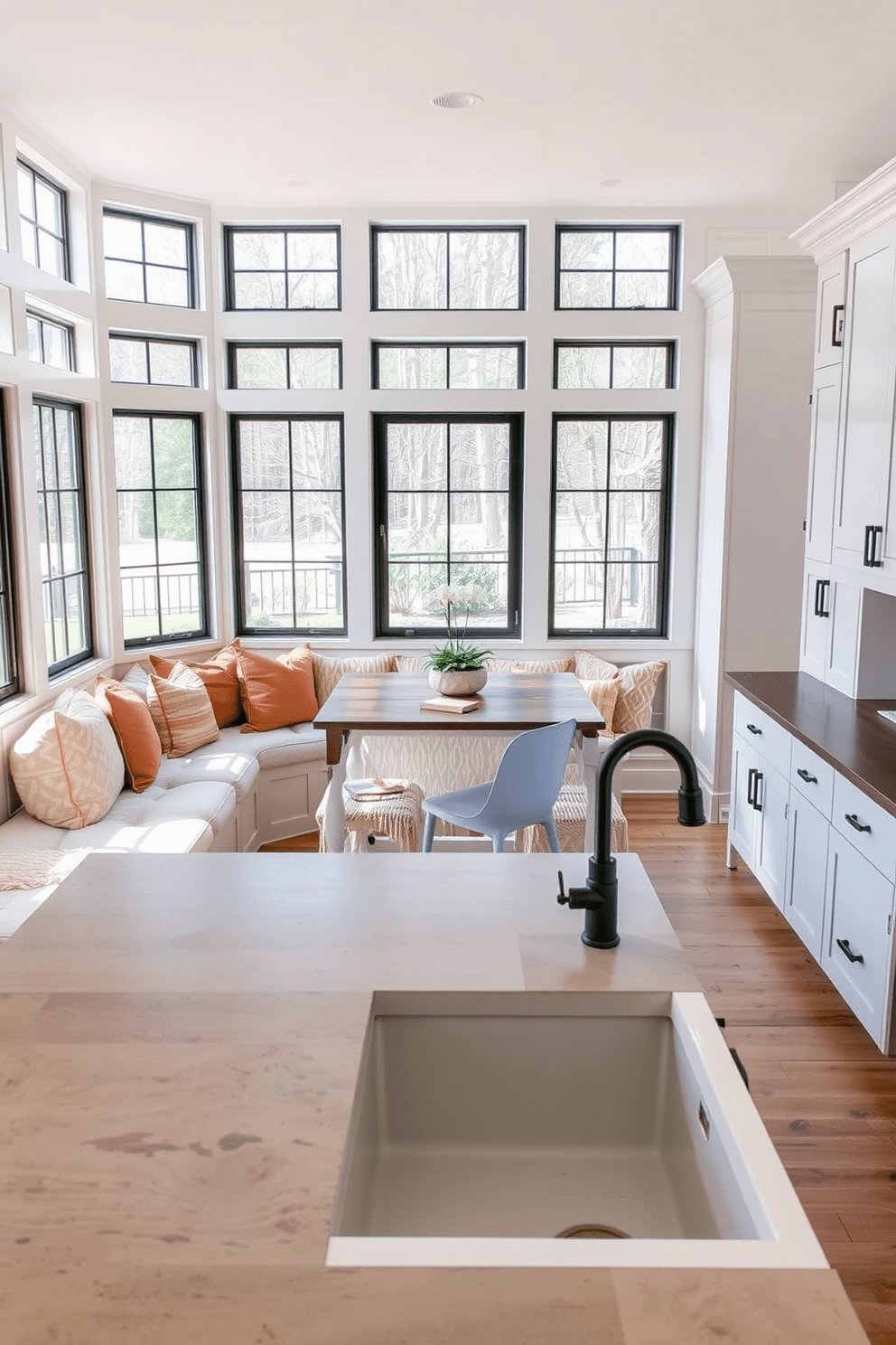 Cozy nook with built-in seating. The nook features a plush, L-shaped bench upholstered in soft, neutral fabric, surrounded by large windows that allow natural light to flood the space. Decorative pillows in warm tones are scattered across the bench, inviting relaxation. A rustic wooden table sits in the center, perfect for morning coffee or casual meals. Farmhouse kitchen design ideas. The kitchen showcases a large, central island made of reclaimed wood, paired with vintage-style bar stools. Shaker-style cabinets in a soft white finish line the walls, accented by matte black hardware and a farmhouse sink with a classic gooseneck faucet.