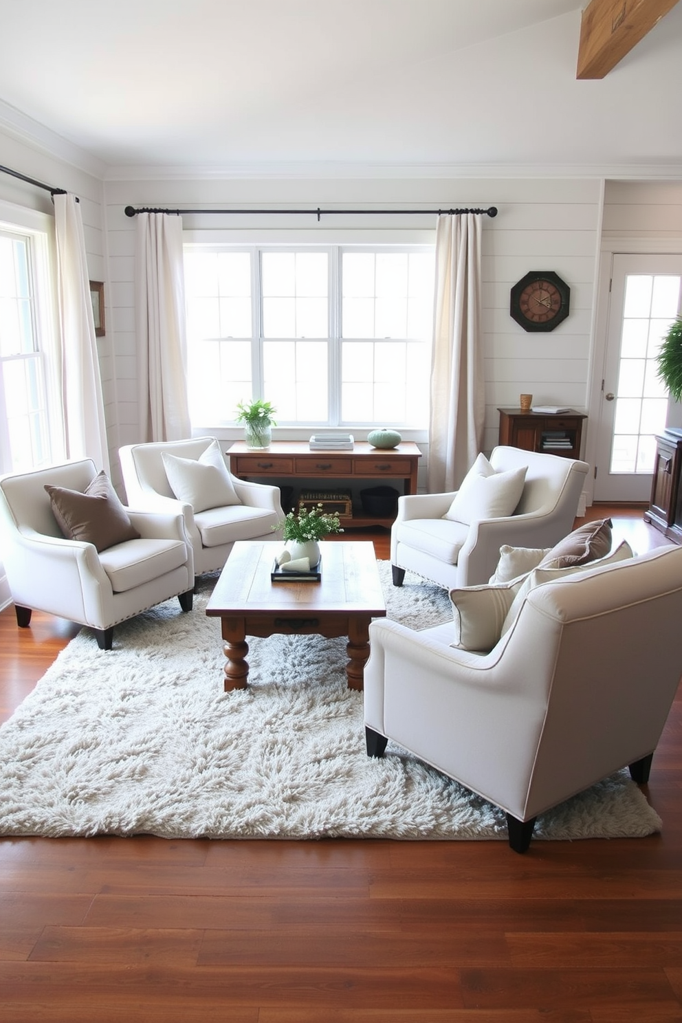 Comfortable armchairs with soft fabric are arranged around a rustic wooden coffee table in a cozy farmhouse living room. The walls are adorned with shiplap paneling and the space is filled with warm, natural light from large windows dressed with simple linen curtains. A plush area rug anchors the seating area, adding texture and warmth to the hardwood floor. Decorative throw pillows in muted tones are scattered on the armchairs, enhancing the inviting atmosphere of the room.