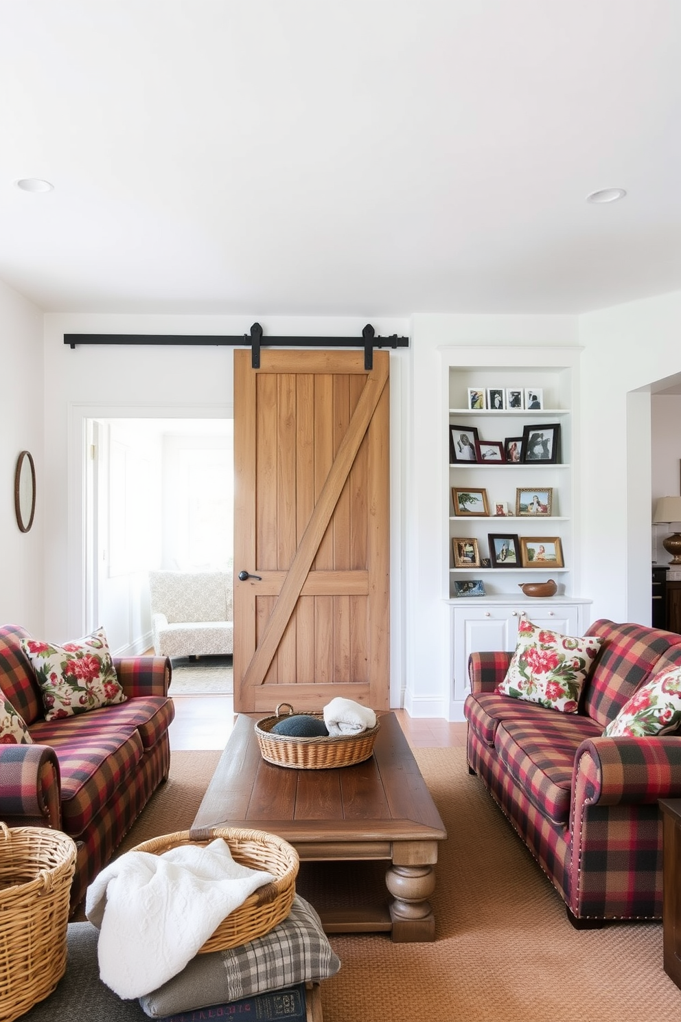 A vintage barn door serves as a charming room divider, adding rustic character to the open space. The living room features a cozy arrangement of overstuffed sofas adorned with plaid and floral patterns, complemented by a reclaimed wood coffee table. The walls are painted in a soft white, creating a bright and airy atmosphere. Decorative elements include a woven basket filled with blankets and a collection of framed family photos on the shelves.