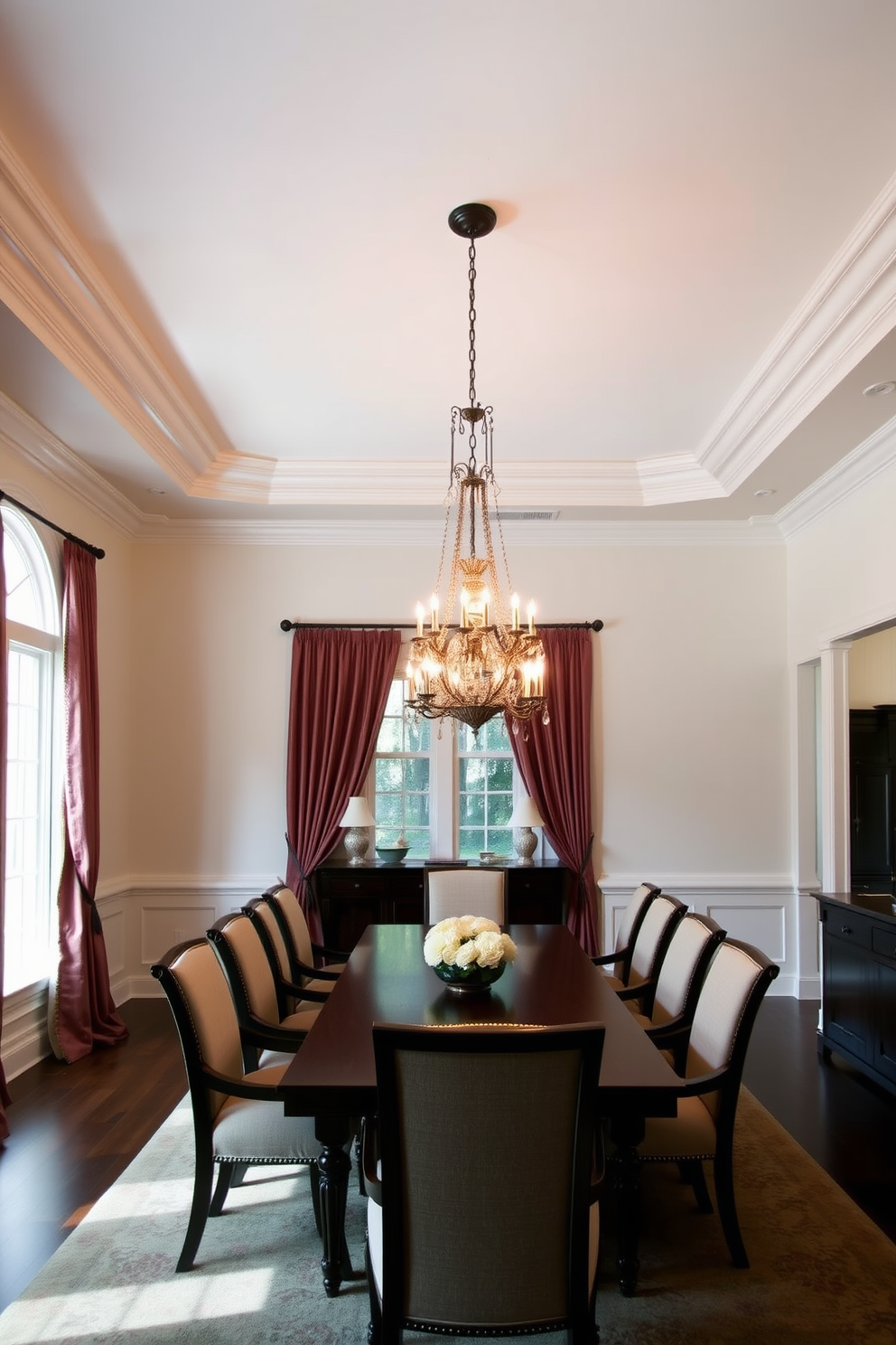 Crown molding adds an elegant touch that enhances the perceived height of the ceiling. The formal dining room features a long wooden table surrounded by upholstered chairs, creating a sophisticated atmosphere. A stunning chandelier hangs from the ceiling, casting a warm glow over the space. The walls are painted in a soft neutral tone, complemented by rich drapes that frame the large windows.