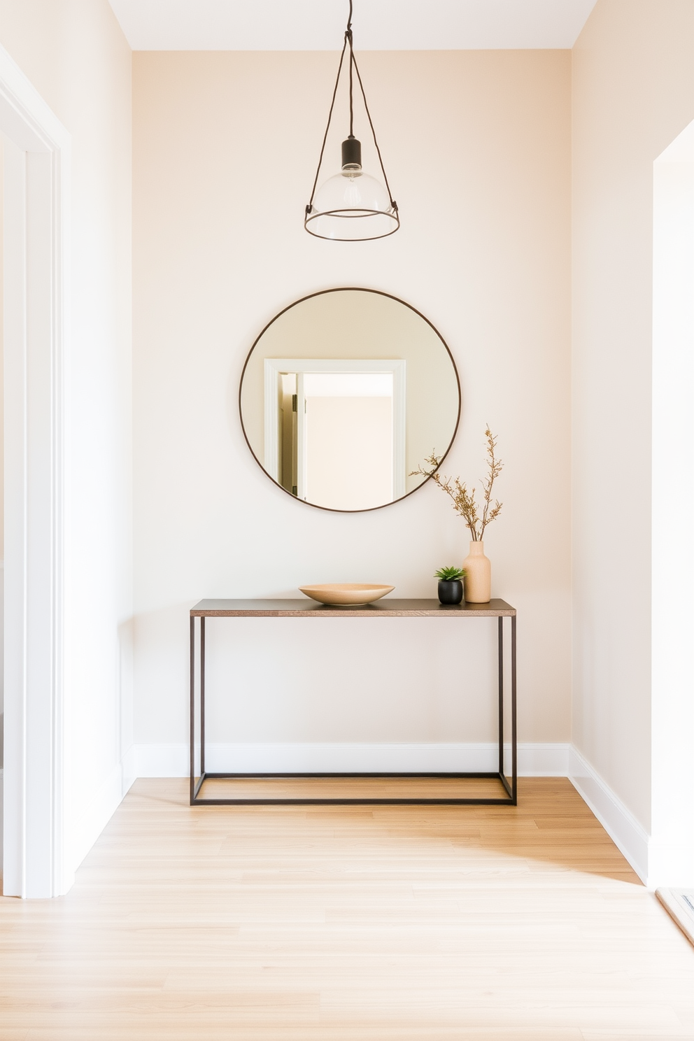 A serene foyer setting that welcomes guests with a soft ambiance. The walls are painted in a light beige hue, complemented by a warm wooden floor that adds a touch of natural elegance. A minimalist console table sits against the wall, adorned with a simple decorative bowl and a small potted plant. A large round mirror hangs above the table, reflecting the soft light from a stylish pendant fixture overhead.