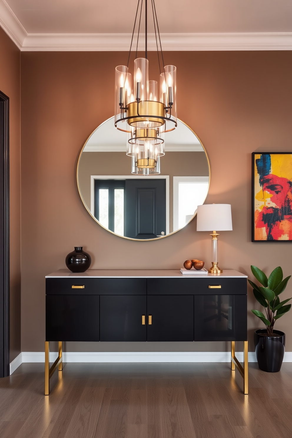 A stylish foyer features a sleek console table made of dark wood with elegant gold accents. Above the table, a large round mirror reflects the soft ambient lighting from a modern chandelier overhead. The walls are painted in a warm taupe, creating a welcoming atmosphere. A vibrant piece of abstract art hangs to the side, while a small potted plant adds a touch of greenery to the space.