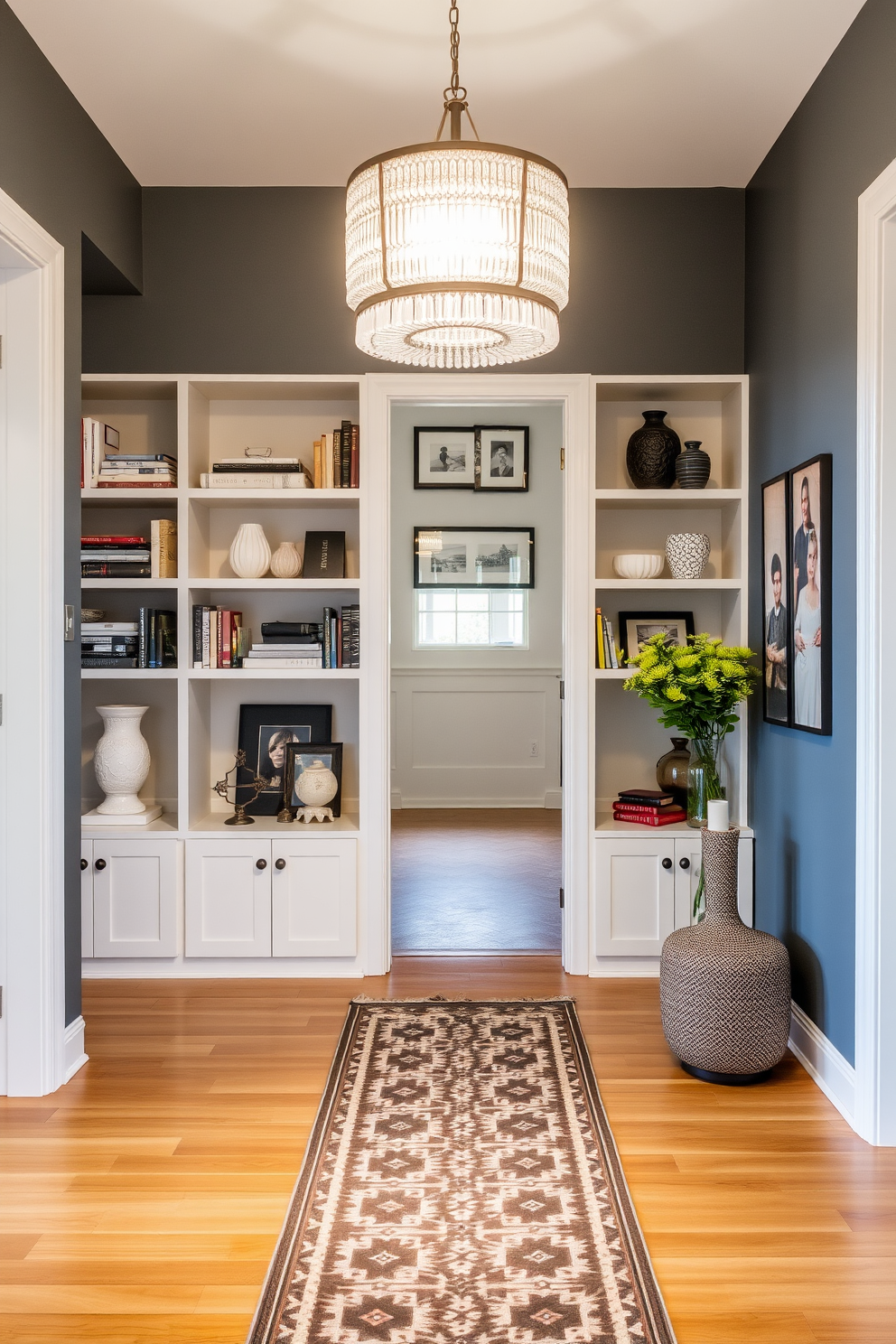 A welcoming foyer entryway features open shelving along one wall, showcasing an array of decorative items such as books, vases, and framed photos. The floor is adorned with a stylish runner rug, and a statement light fixture hangs above, creating an inviting atmosphere.