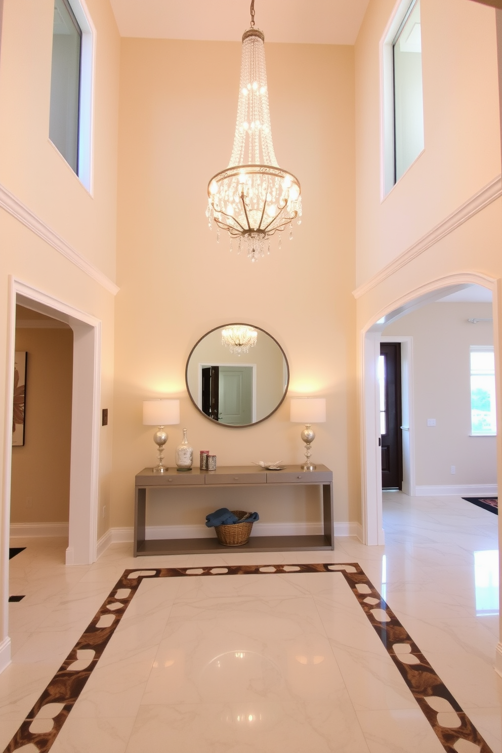 An elegant chandelier hangs from a high ceiling, casting a warm glow over the foyer. The entryway features a stunning marble floor with intricate inlays, complemented by a sleek console table adorned with decorative accents. The walls are painted in a soft cream, providing a bright and inviting atmosphere. A large round mirror above the console reflects the chandelier's light, enhancing the sense of space and elegance.