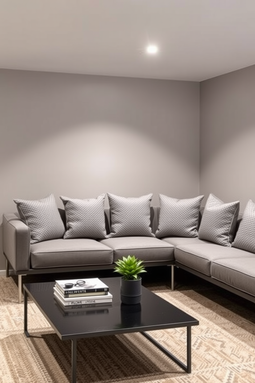 Textured gray cushions are arranged on a modern sectional sofa in a stylish basement lounge. The walls are painted a soft gray, creating a cozy and inviting atmosphere. A sleek coffee table sits in front of the seating area, topped with decorative books and a small potted plant. Ambient lighting fixtures provide a warm glow, enhancing the overall aesthetic of the space.