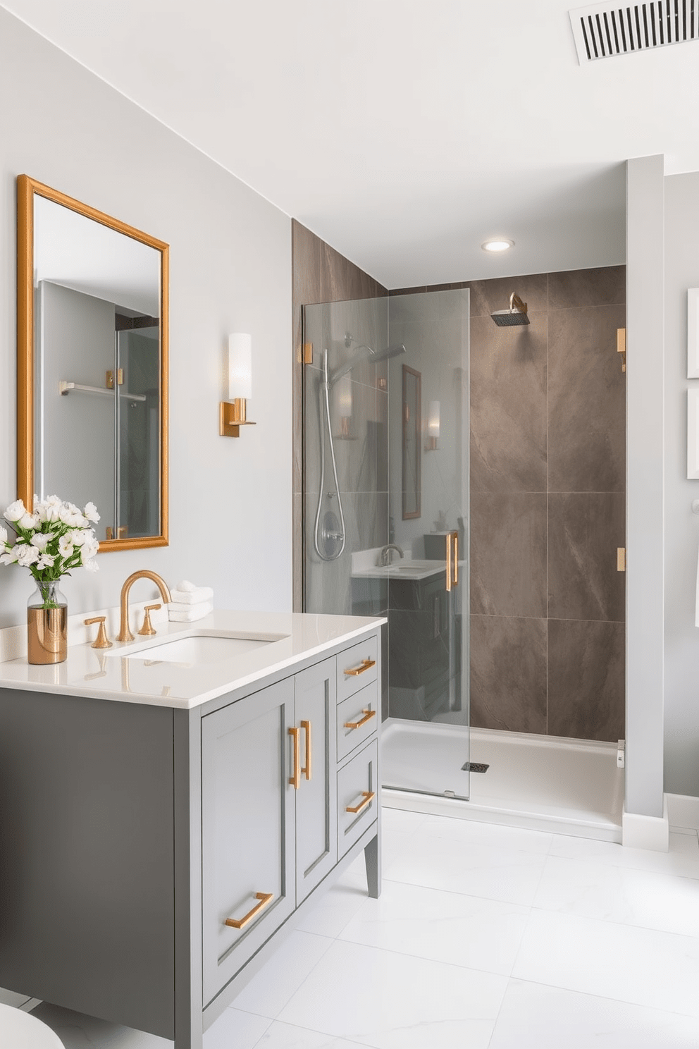 A sleek gray vanity with gold hardware sits prominently in the center of the bathroom. The walls are adorned with soft gray tones that complement the elegant fixtures and create a serene atmosphere. A spacious walk-in shower features frameless glass doors and modern rainfall showerhead. The floor is covered in large white tiles that enhance the overall brightness of the space.