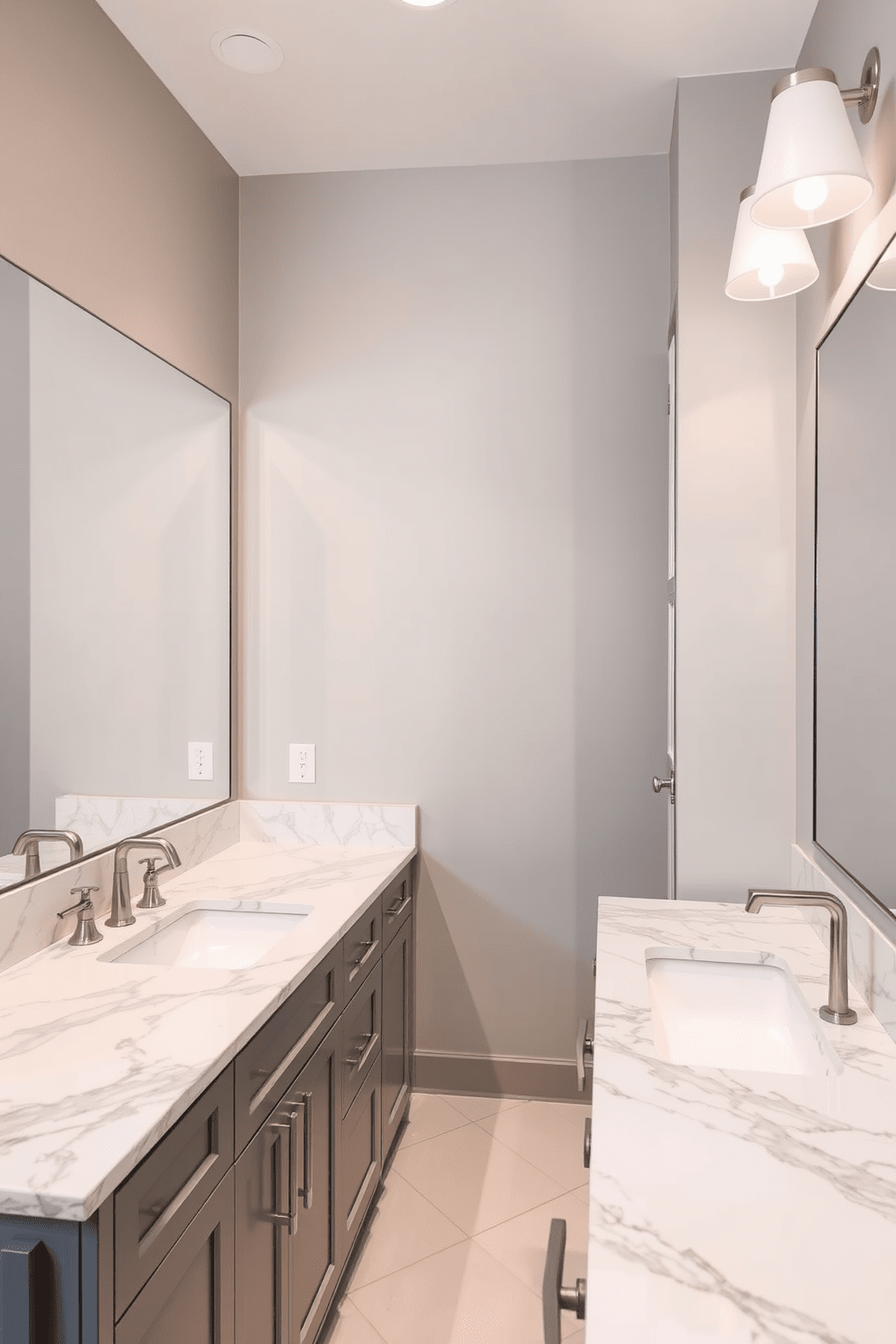 A modern bathroom featuring sleek marble countertops paired with elegant gray cabinetry. The space is accented with brushed nickel fixtures and a large frameless mirror that enhances the room's brightness. The walls are painted in a soft gray hue, creating a serene atmosphere. Stylish lighting fixtures provide warm illumination, complementing the overall design aesthetic.