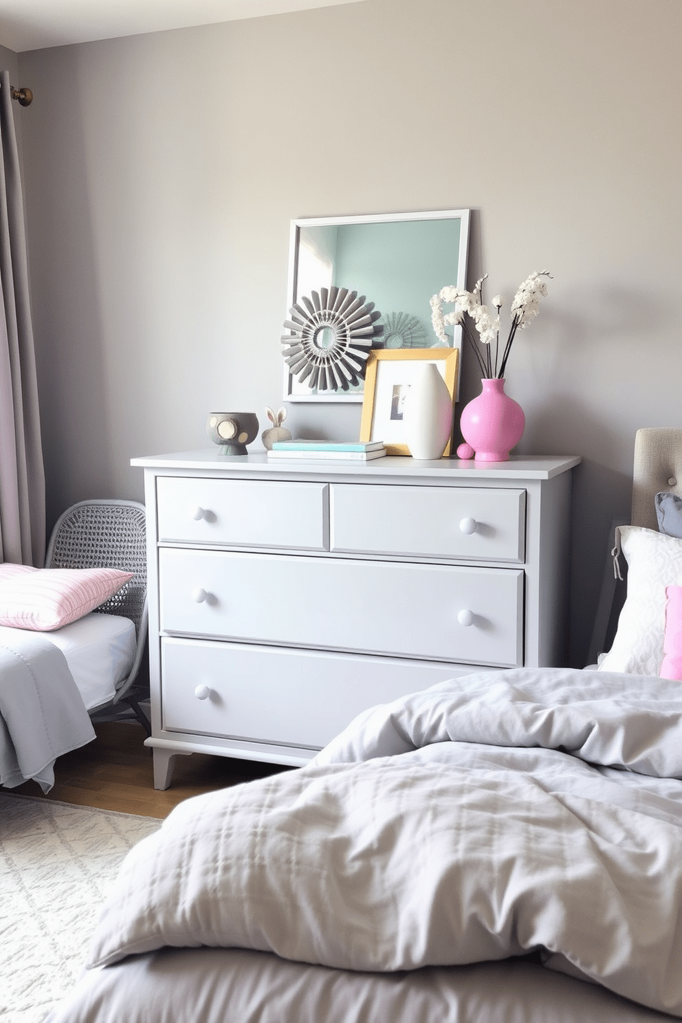 A pastel gray dresser is the focal point of the room, adorned with vibrant accessories that add a pop of color. The bedroom features soft gray walls, complemented by cozy bedding in varying shades of gray and pastel accents.